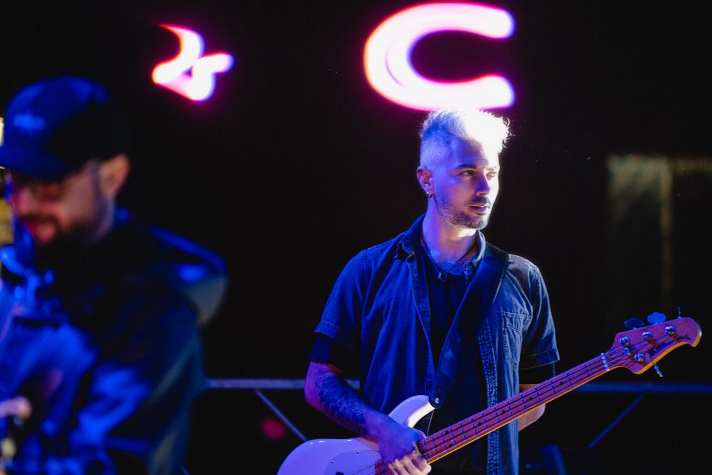 Musicista suona basso elettrico sul palco illuminato.