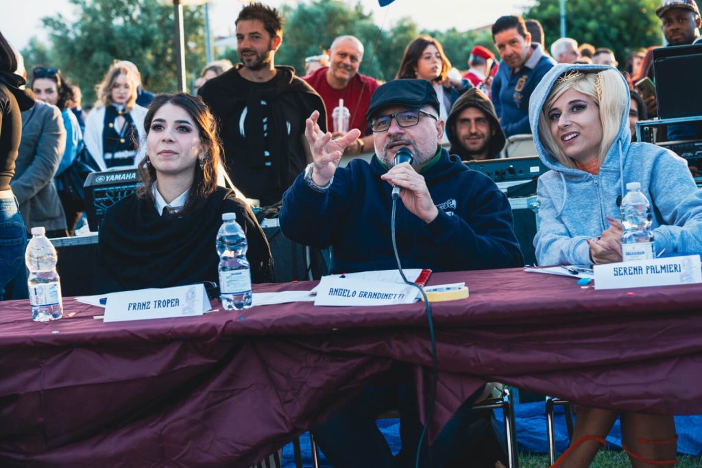 Giuria durante evento con microfono e pubblico.