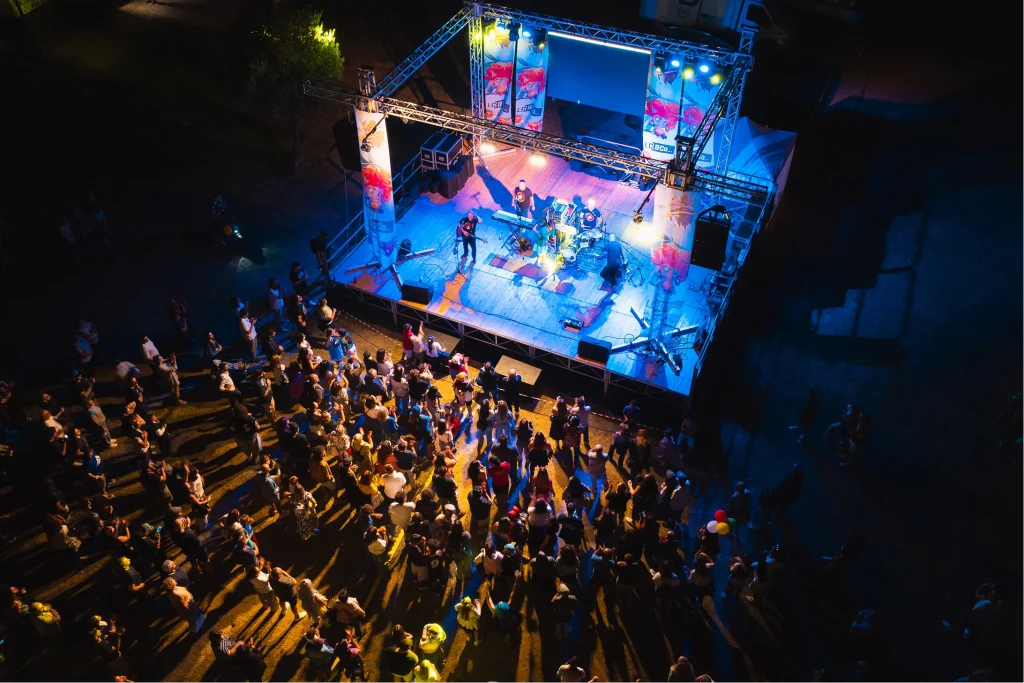 Concerto all'aperto notturno con folla e palco illuminato